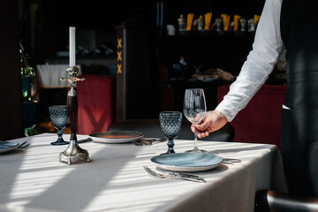 A young waiter in a stylish uniform is engaged in serving the table in a beautiful gourmet restaurant close-up. Table service in the restaurant.