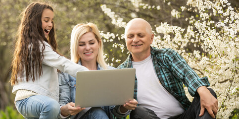 Happy different generations affectionate family having fun indoors, looking at laptop screen, enjoying watching funny comedian movie or recollecting memories with vacation photos on electronic device