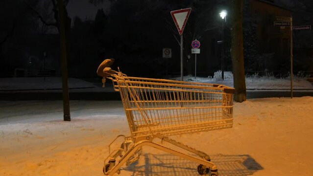 An empty cart from a supermarket on the street on a dark winter evening in the light of lanterns