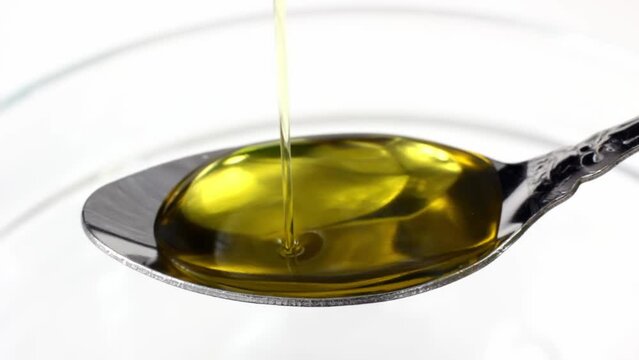 Yellow organic olive oil pouring into the spoon close up