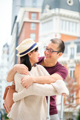 Obraz premium Multiracial couple of tourists smiling, hugging and looking at each other. Sightseeing in Madrid, Spain.
