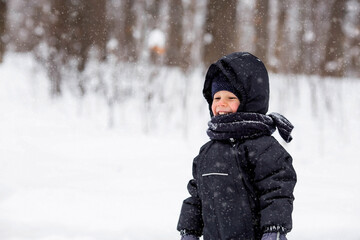 Portrait of a beautiful little Russian boy in winter in the park. Snow is falling. Cold. Red cheeks. The concept of a happy childhood and remedies for the skin from frost.