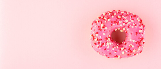 Pink donut with sprinkles on pink pastel background. One sweet pink donut. Top view. Copy space