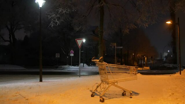 An empty cart from a supermarket on the street on a dark winter evening in the light of lanterns