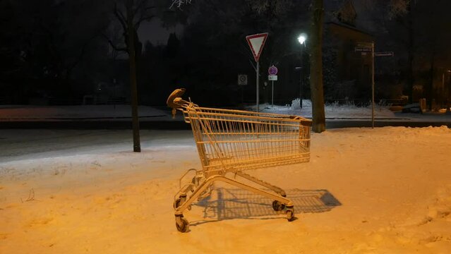 An empty cart from a supermarket on the street on a dark winter evening in the light of lanterns