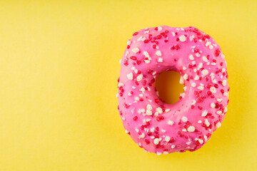 Fototapeta na wymiar Strawberry donut with pink icing and sprinkles. Sweet pink donut on yellow background. Flat lay. Copy space