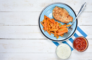 Top view of healthy fitness food, carrot fries, slice of chicken steak. homemade garlic dip and hot tomato sauce with chili. Light blue plate on white board wooden desk. View from above