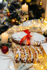 Traditional German Christmas stollen made of dried fruits and nuts, sprinkled with powdered sugar on the background of a Christmas decor with candles. A festive treat.