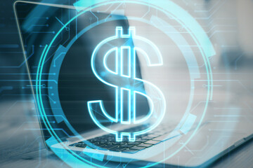 Close up of desktop with laptop and glowing dollar sign on blurry background. Money and online...