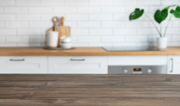 Dark wooden countertop with free space for mounting a product or layout against the background of a blurred white kitchen  with plant.
