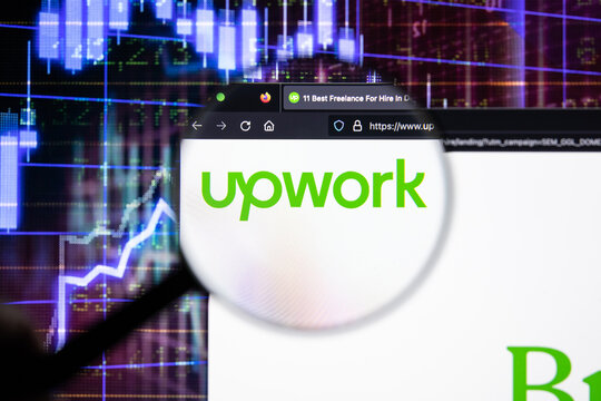 Upwork company logo on a website with blurry stock market developments in the background, seen on a computer screen through a magnifying glass