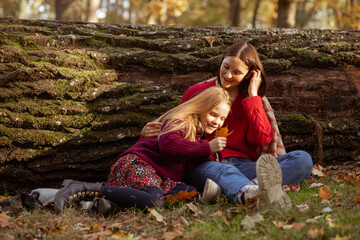 Laughing, joyful relaxed mother and daughter, woman and girl lie, hug near tree trunk with green moss during exploration