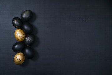 Eggs painted gold and black on dark wooden background. Minimal Easter concept. Luxury backdrop with copy space for text.