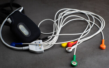 Holter, a medical blood pressure monitor for a heart rate measurement with all the colorful cables on industrial gray background