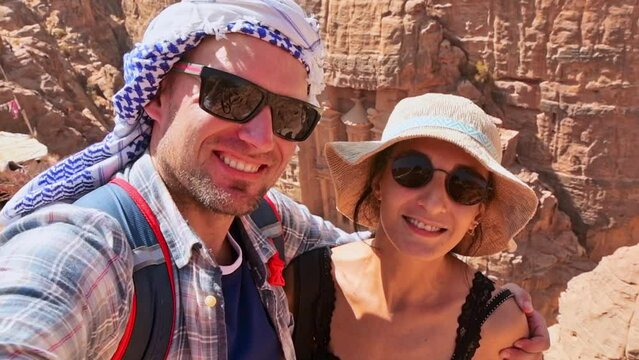Caucasian couple tourist on viewpoint in Petra ancient city over Treasury or Al-khazneh take smartphone photo together. Jordan, one of seven wonders. UNESCO World Heritage site.
