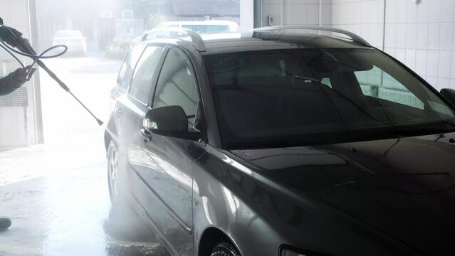 Self service car wash. Somebody washes off soap with water from the car. Close-up. Professional cleaning. Side view. High pressure gun. Slow motion. Transport industry. Cleaning auto service. Nobody.