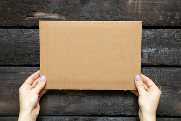 A woman's hand holds a cardboard box in her hands on a wooden background, space for text, a...