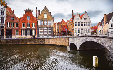 Naklejka premium Bruges Belgium vintage stone houses and bridge over canal ancient medieval street picturesque landscape in summery sunny day with blue sky white clouds