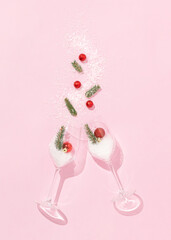 Christmas layout made of two wine glasses with red Christmas balls, fir branches and snow on bright pink background. Minimal New Year celebration concept. Creative winter party aesthetic.