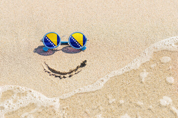 Fototapeta na wymiar A painted smile on the beach and sunglasses with the flag of Bosnia and Herzegovina.