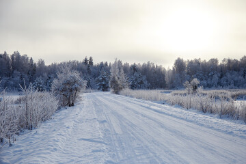 Fototapeta na wymiar Winter landscape with snowy road and forest covered with hoar frost, selective focus