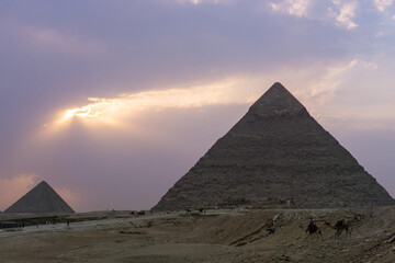 Fototapeta na wymiar Sunset at the pyramids of Giza, Pyramid of Kefren in the foreground and Pyramid of Menkaure at the end of the shot, purple sky with clouds.