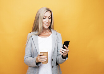 Happy mature old 60s woman with long hair holding smartphone and takeaway coffee