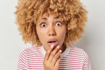Close up portrait of shocked woman stunned after hearing something keeps hand on lips and looks...