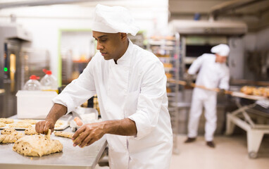 man in chefs uniform kneading dough in bakery