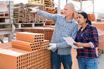 Colleagues man and woman collecting order of red bricks at warehouse of building materials