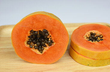 half of ripe papaya fruit with seeds on wooden board .