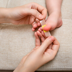 Mother woman sticks a medical adhesive plaster on the toddler baby leg. Mom s hand with sticky wound protection tape and child s foot. Kid aged one year and three months
