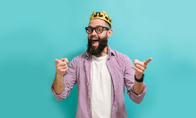 Portrait of a young attractive man with a beard stylishly dressed with a golden crown on his head...