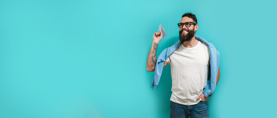 Young handsome hipster man with a beard holds a paper airplane in his hand, smiling happily.