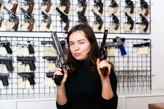 Emotional woman with two revolvers in hands in a gun shop