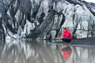 Man in red jacket on the shore of the glacier lagoon in the background