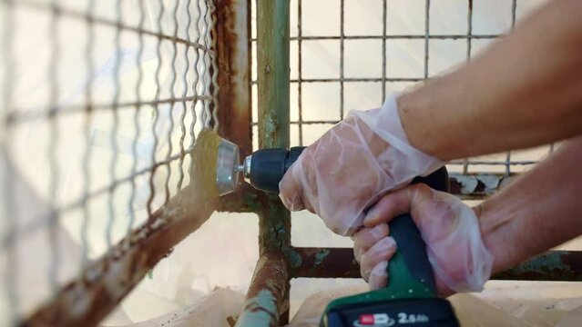 Workman using electrical grinder with metal brush nozzle for removing heavy corrosion and old paint from metal surface, worker grinding old metal texture, removing of rust before applying