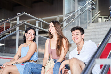 Portrait of diverse college friends sitting on station stairs - Happy multiracial group of young people having fun and relaxing - Friendship, youth and traveler concept
