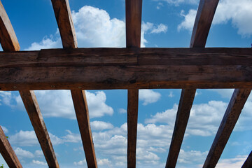 An incomplete wooden roof skeleton in nature with sky and clouds frame, tree branches in the sky....