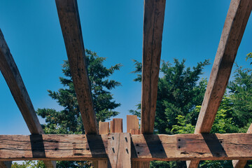An incomplete wooden roof skeleton in nature with sky frame, tree branches in the sky. roof repair.