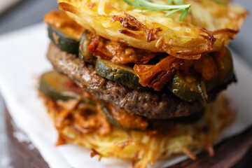 Burger with vegetables and potato patty on table
