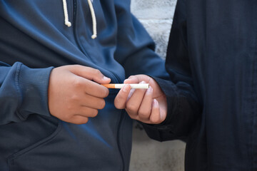 Boy learning to smoke with the same age friends in the area behind the school fence which teachers cannot see, bad influence of secondary school or junior high school life, addiction.