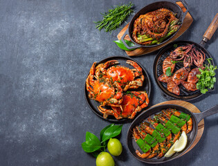 Obraz na płótnie Canvas Set of Seafood Dishes. Crabs, octopus, squids and tiger shrimps on cast iron pans and plates on a black background. Top view. Copy space for text.