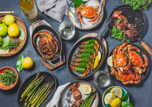 Set table with seafood dishes - cooked crabs, tiger shrimps, grilled octopus and squids on cast iron grilled pans and plates, White wine. Toned photo. Top view