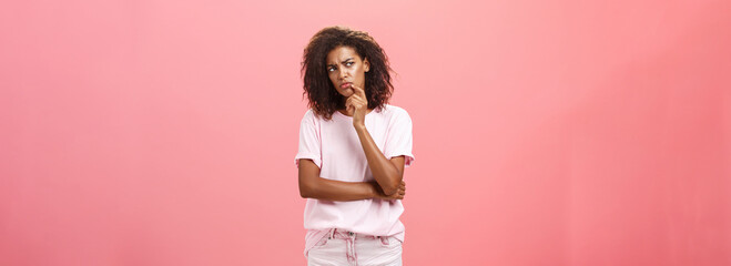 Suspicious displeased dark-skinned young curly-haired woman in trendy t-shirt and shorts saying hmm...