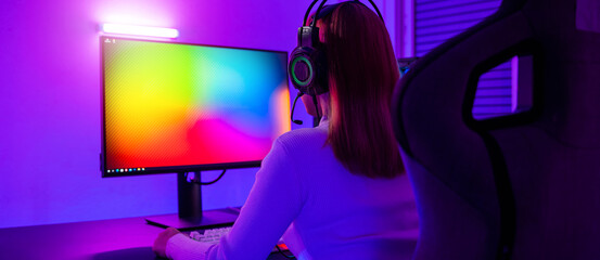 Asian professional gamer playing online video game on desktop computer PC have colorful neon LED lights, young woman in gaming headphones using computer for playing game at home © sorapop
