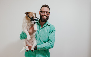 Handsome hipster guy with a beard hugs his cute dog Jack Russell Terrier on a gray background....