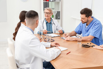 Fototapeta premium Medical conference. Team of doctors listening to speaker at wooden table in clinic