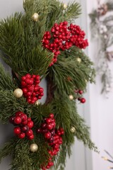Naklejka na ściany i meble Beautiful Christmas wreath with red berries and decor hanging on white door, closeup