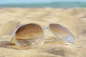 Fototapeta na wymiar Stylish sunglasses on sandy beach near sea, closeup